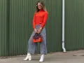 Modna kobieta w pomarańczowym golfie i kraciastych kulotach, białych kozaczkach i okularach. Stylowe kuloty stylizacje.