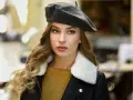 Elegancka kobieta w grafitowym beretcie, pokazująca, jak się nosi beret, z burzą blond loków i w stylowej kurtce.