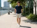 Mężczyzna w granatowym polo i beżowych szortach, prezentujący masywne uda stylizacje, spaceruje promenadą.