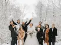 Radosna para młoda i goście rzucają śnieżkami na tle zimowego lasu. Idealne stylizacje na wesele zimą.