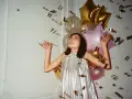 Kobieta w srebrnej sukience cieszy się deszczem złotych konfetti. Balony tworzą tło dla tego radosnego, tematycznego sylwestra.