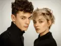 Młoda para, on z kręconymi włosami, ona z blond pixie cut, w czarnych golfach. Ich spojrzenia sugerują, że tworzą idealny **matching** duet.