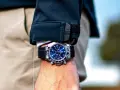 Elegancki zegarek na bransolecie z niebieską tarczą, noszony na nadgarstku pod czarną kurtką. Stylowy sposób na noszenie zegarka.