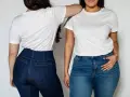 Dwie kobiety w białych T-shirtach i dżinsach. Jedna z nich ma podkreślone szerokie biodra w dopasowanych spodniach.