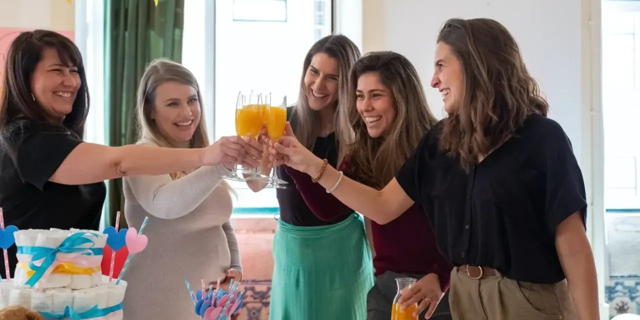 Kobiety świętują baby shower, wznosząc toasty. Widać tort z pieluch i dekoracje. Idealny strój na baby shower to coś wygodnego i eleganckiego.