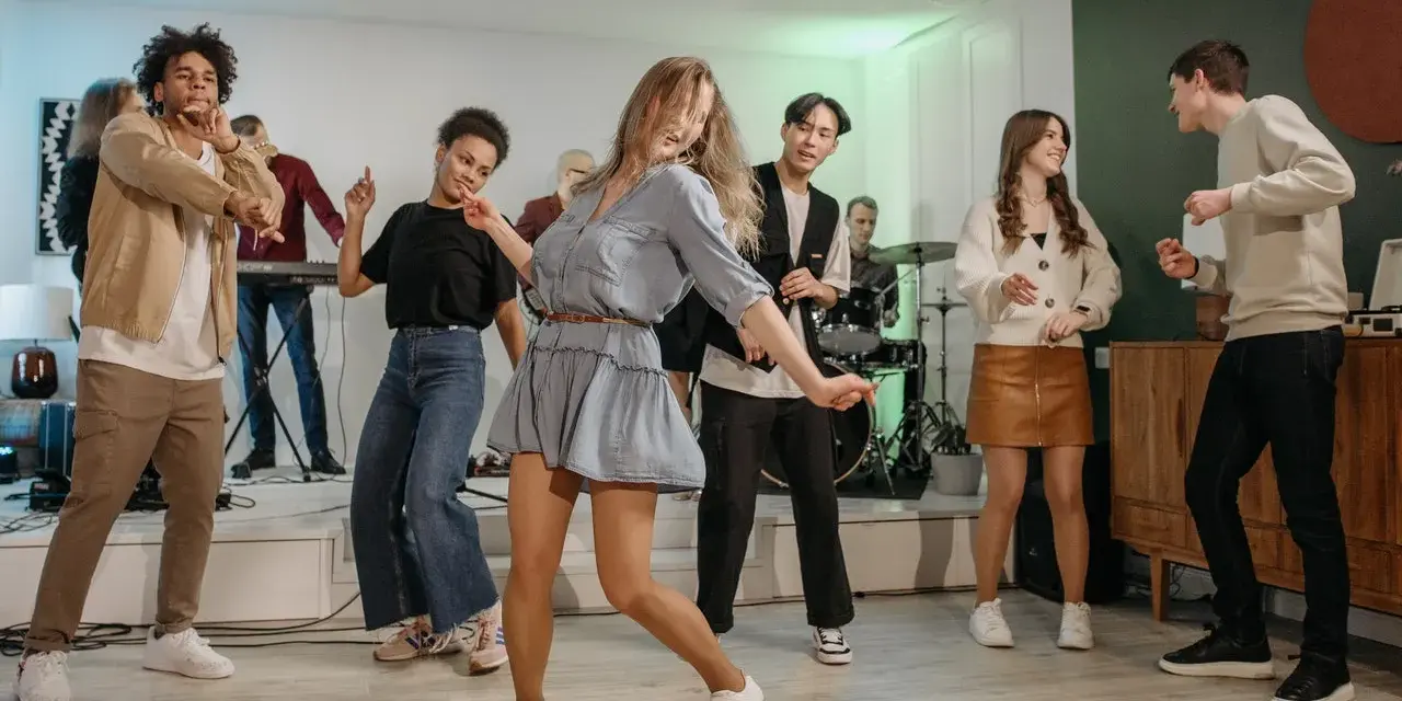 Luźne stylizacje na domówkę: jeansy, sukienka i wygodne buty. Wszyscy tańczą i świetnie się bawią.