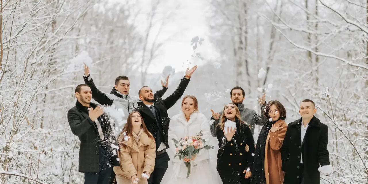 Radosna para młoda i goście rzucają śnieżkami na tle zimowego lasu. Idealne stylizacje na wesele zimą.