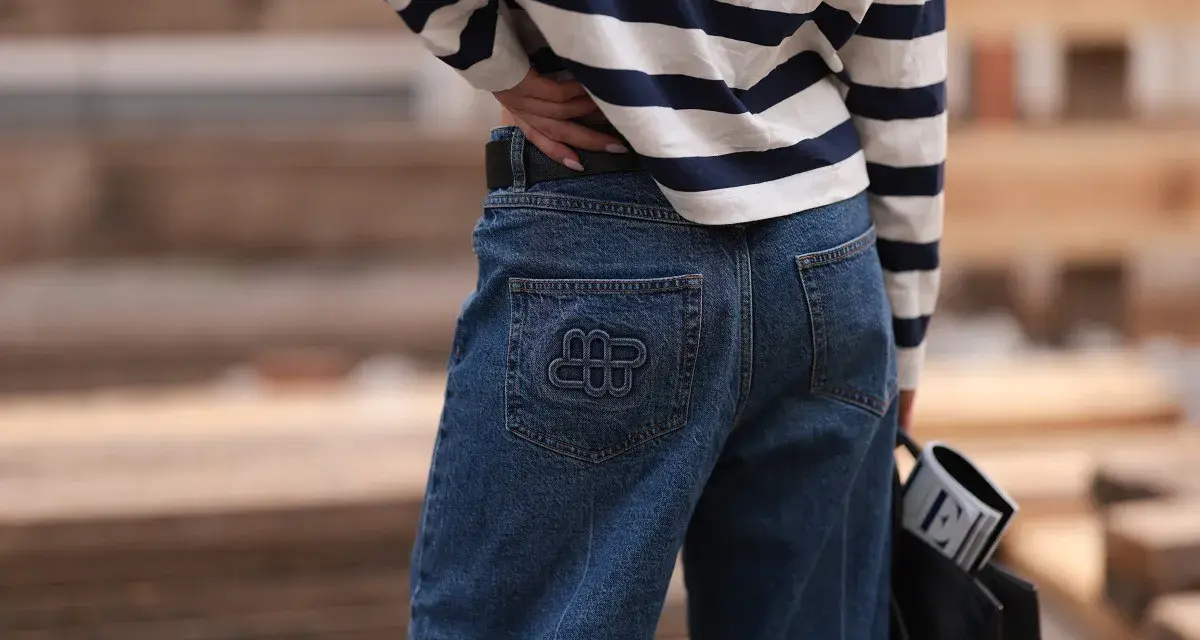 Kobieta w granatowych jeansach z logo i bluzce w paski. Idealne spodnie dla niskich kobiet, które podkreślą sylwetkę.