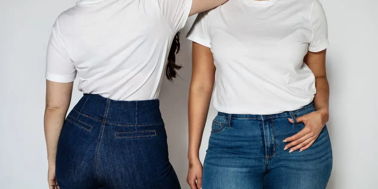 Dwie kobiety w białych T-shirtach i dżinsach. Jedna z nich ma podkreślone szerokie biodra w dopasowanych spodniach.