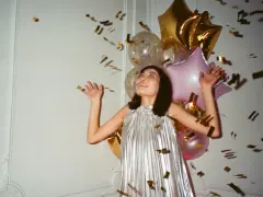 Kobieta w srebrnej sukience cieszy się deszczem złotych konfetti. Balony tworzą tło dla tego radosnego, tematycznego sylwestra.