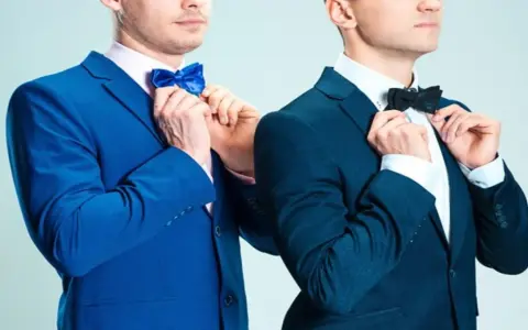 Dwóch mężczyzn w granatowych garniturach poprawia muszki. Jeden w niebieskiej, drugi w czarnej. Jaka mucha do granatowego garnituru?