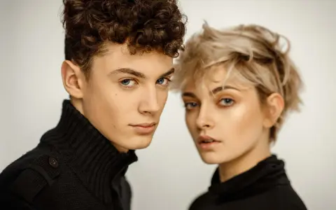 Młoda para, on z kręconymi włosami, ona z blond pixie cut, w czarnych golfach. Ich spojrzenia sugerują, że tworzą idealny **matching** duet.