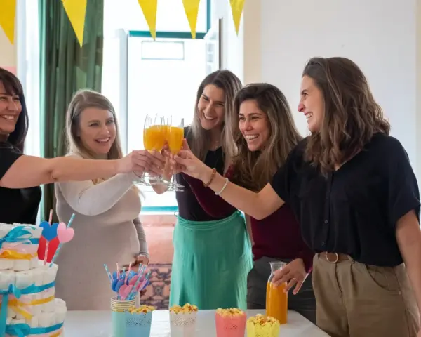 Kobiety świętują baby shower, wznosząc toasty. Widać tort z pieluch i dekoracje. Idealny strój na baby shower to coś wygodnego i eleganckiego.