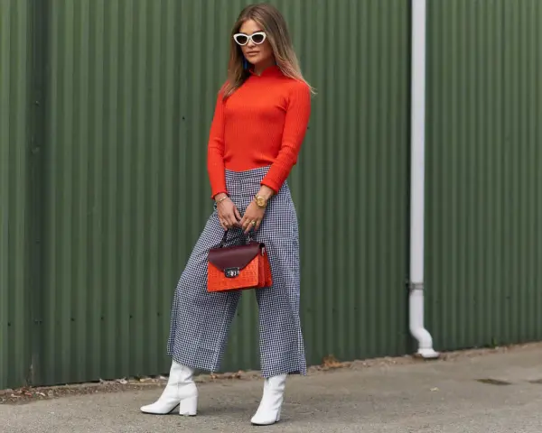 Modna kobieta w pomarańczowym golfie i kraciastych kulotach, białych kozaczkach i okularach. Stylowe kuloty stylizacje.