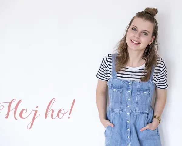 Uśmiechnięta dziewczyna w stylu normcore, w jeansowej sukience na szelkach i pasiastym t-shircie, z napisem "Hej ho!".