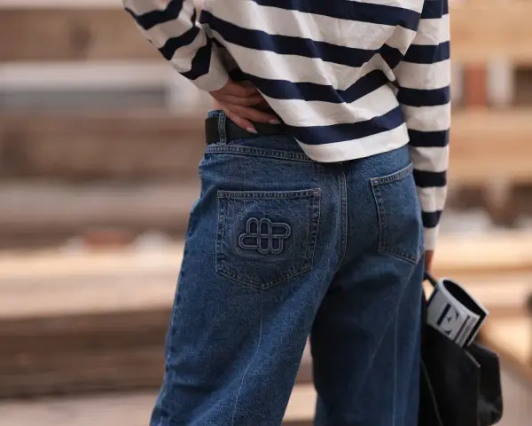 Kobieta w granatowych jeansach z logo i bluzce w paski. Idealne spodnie dla niskich kobiet, które podkreślą sylwetkę.