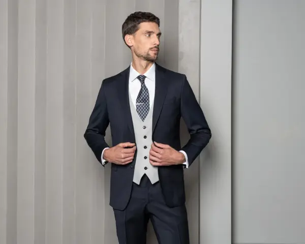 Mężczyzna w granatowym garniturze, jasnej kamizelce i wzorzystym krawacie. Elegancki wybór: krawat czy mucha?