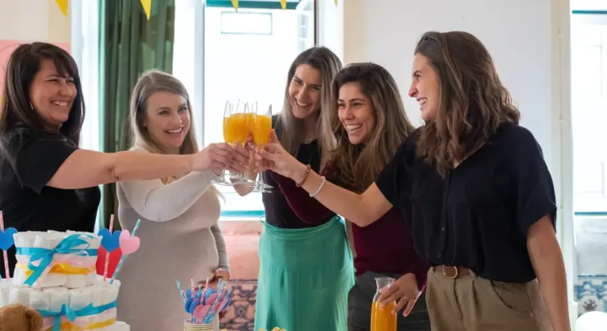 Kobiety świętują baby shower, wznosząc toasty. Widać tort z pieluch i dekoracje. Idealny strój na baby shower to coś wygodnego i eleganckiego.