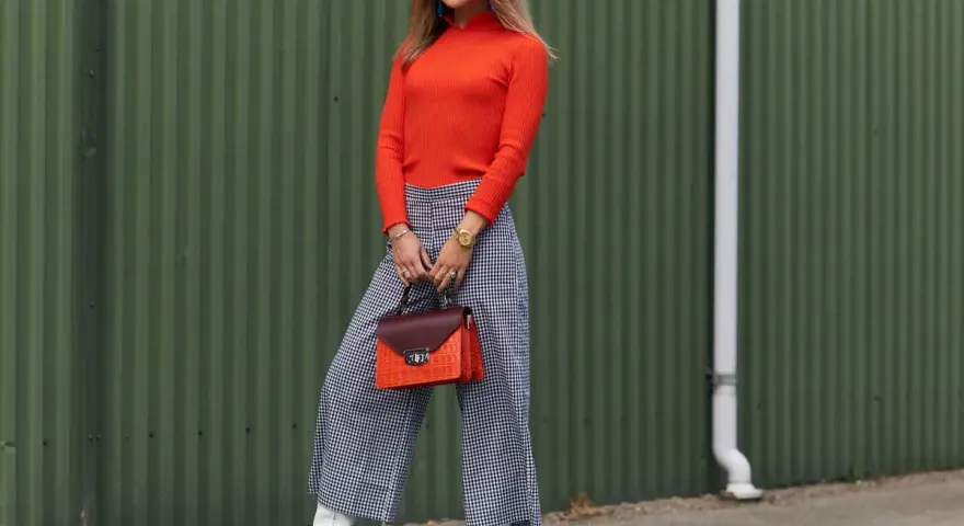Modna kobieta w pomarańczowym golfie i kraciastych kulotach, białych kozaczkach i okularach. Stylowe kuloty stylizacje.