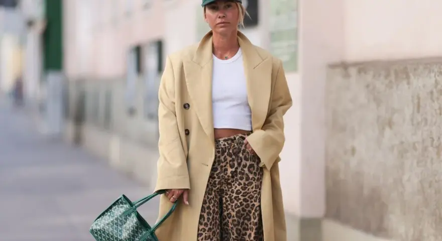 Modna kobieta w beżowym płaszczu i spodniach w panterkę. Stylowe spodnie w panterkę to klucz do odważnych stylizacji.