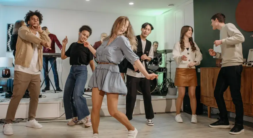 Luźne stylizacje na domówkę: jeansy, sukienka i wygodne buty. Wszyscy tańczą i świetnie się bawią.