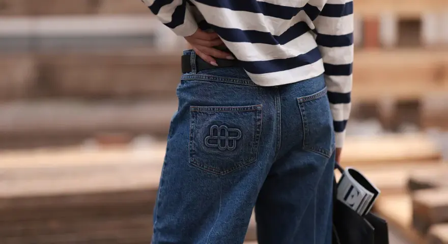 Kobieta w granatowych jeansach z logo i bluzce w paski. Idealne spodnie dla niskich kobiet, które podkreślą sylwetkę.