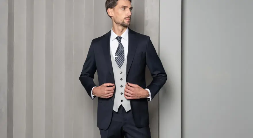 Mężczyzna w granatowym garniturze, jasnej kamizelce i wzorzystym krawacie. Elegancki wybór: krawat czy mucha?