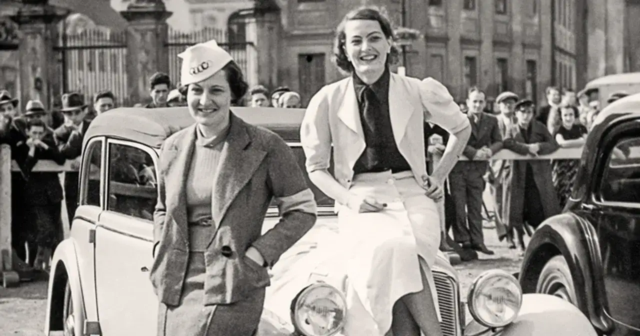 Dwie kobiety w stylowych strojach z lat 30. XX wieku pozują przy samochodzie. Elegancka moda damska tamtych lat.