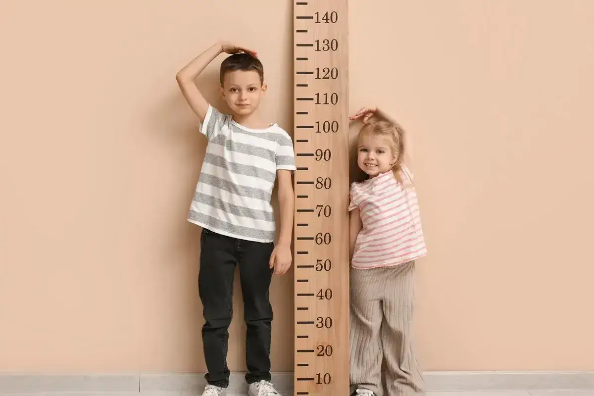 Chłopiec i dziewczynka mierzą wzrost. Chłopiec ma ok. 134 cm, co sugeruje wiek 8-9 lat.