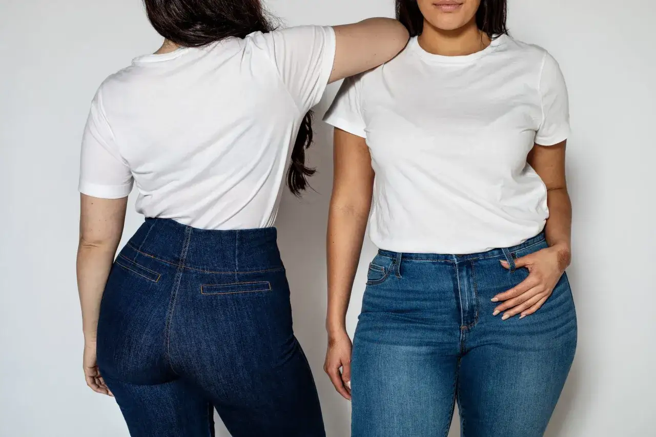 Dwie kobiety w białych T-shirtach i jeansach. Jedna z nich ma podkreślone szerokie biodra.