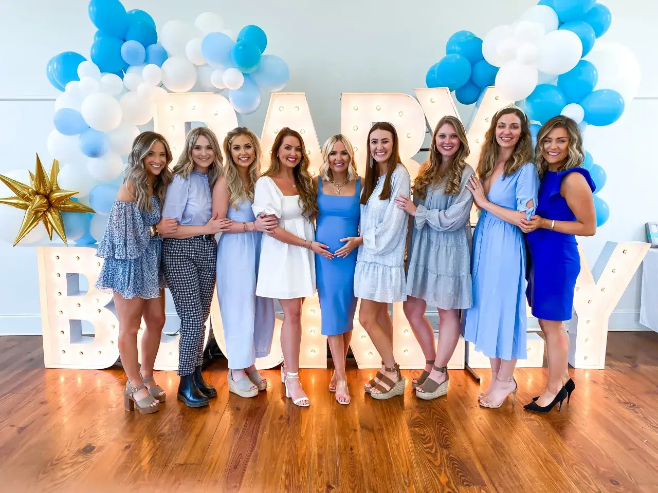 Grupa kobiet w niebieskich i białych strojach na baby shower. Inspiracja, jak się ubrać na baby shower, w pastelowych kolorach i eleganckich sukienkach.