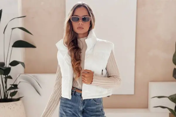 Modna kobieta w białej kamizelce i okularach przeciwsłonecznych prezentuje stylowe stylizacje z kamizelką.
