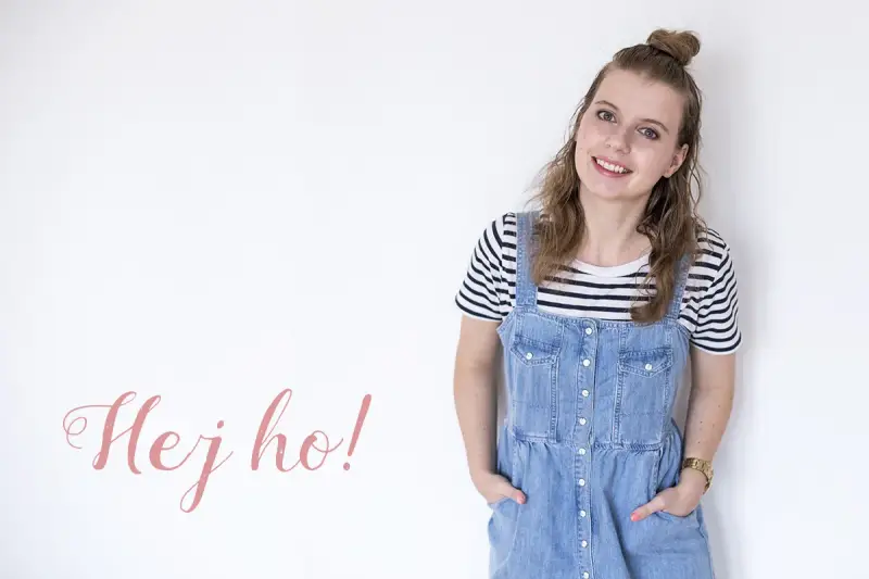 Uśmiechnięta dziewczyna w stylu normcore, w jeansowej sukience na szelkach i pasiastym t-shircie, z napisem "Hej ho!".